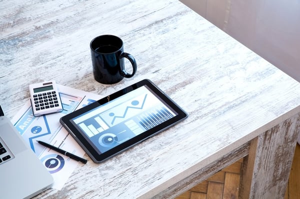 A tablet on a desk next to a laptop, calculator, and coffee mug