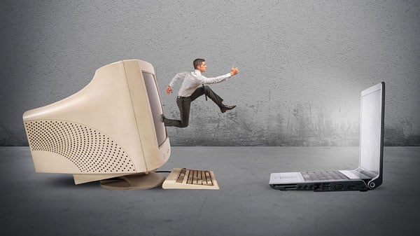 Man jumping out of an old computer desktop into a newer laptop computer